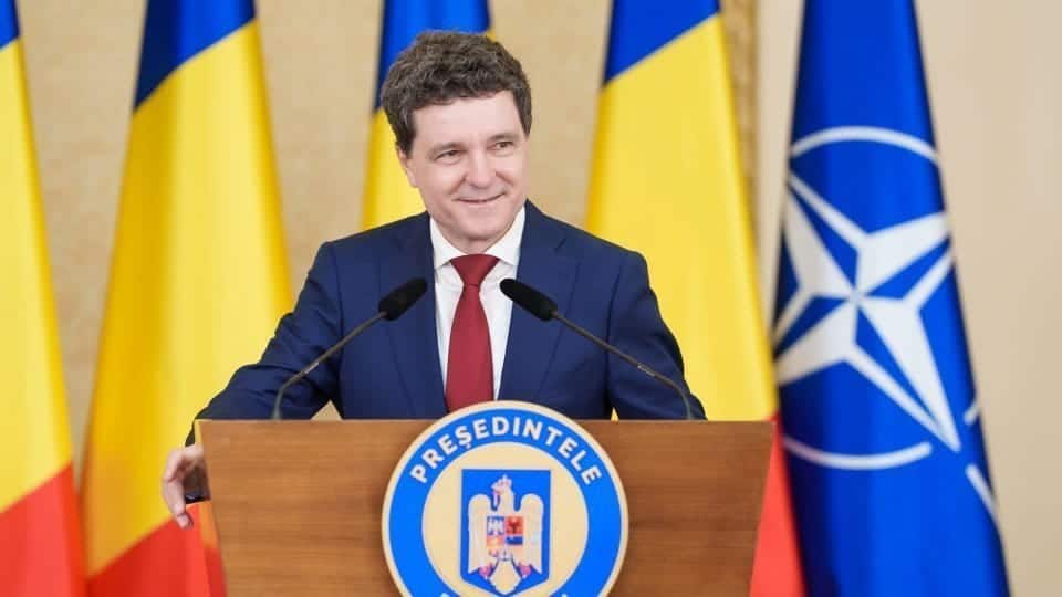 1. Lider român la conferință politică cu drapeluri naționale și NATO în fundal.